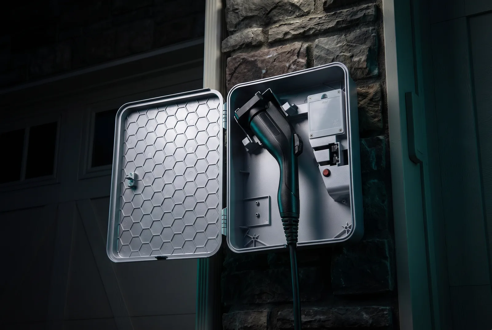 EVchargeME lockbox open on a dark stone wall, honeycomb lid pattern visible, J1772 connector plugged in under teal accent lighting