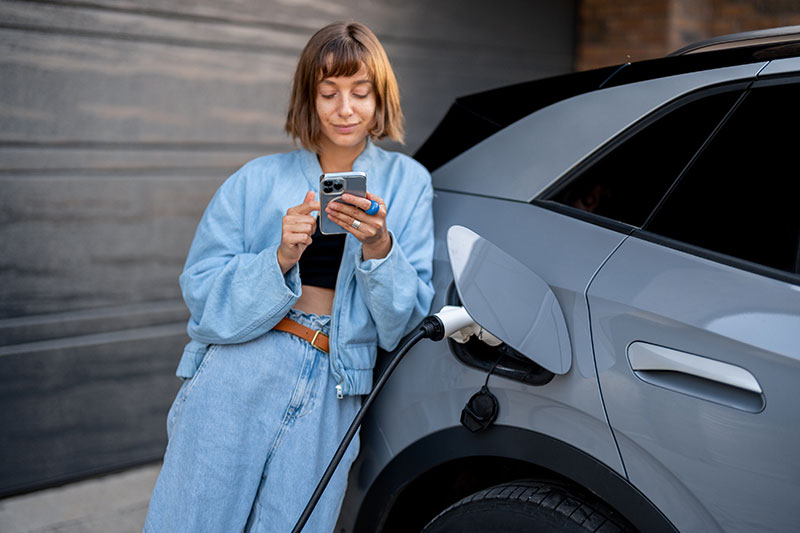 woman leaning against her charging EV using her phone